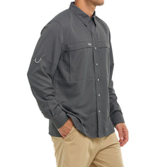 Man wearing a dark gray long-sleeve outdoor shirt with tan pants, standing with hand in pocket.