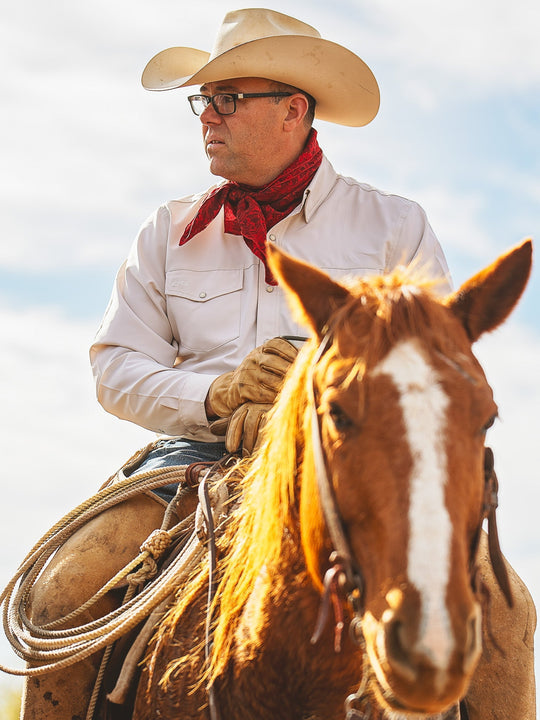 Man in cowboy hat and scarf riding a horse with a clear sky background