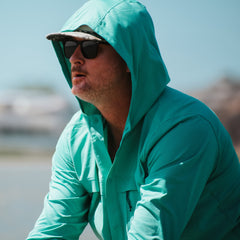 Man wearing a teal hooded jacket and sunglasses outdoors
