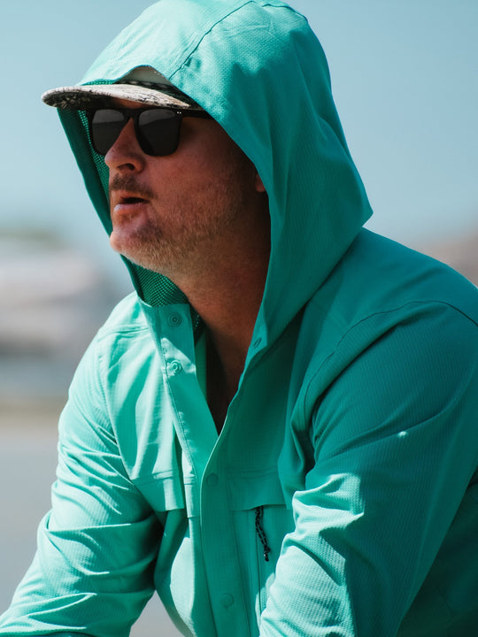 Man wearing a teal hooded jacket and sunglasses outdoors