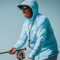 Man wearing a light blue hooded jacket holding a fishing rod against a clear sky.