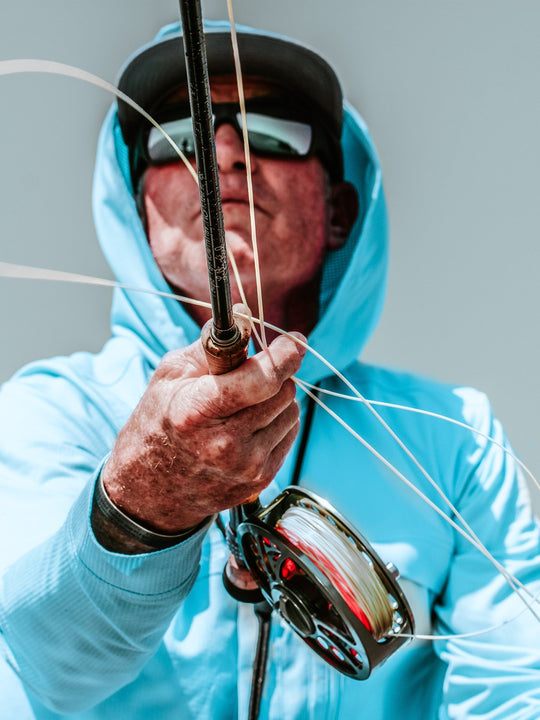 Person in a light blue hoodie holding a fishing rod with a gray background