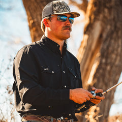 Man in outdoor setting holding a fishing rod, wearing sunglasses and a cap.