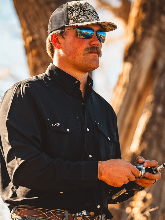 Man in outdoor setting holding a fishing rod, wearing sunglasses and a cap.