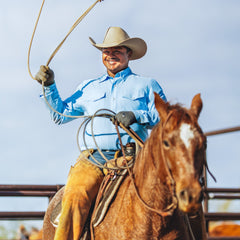 Man on horseback holding a lasso against a clear sky